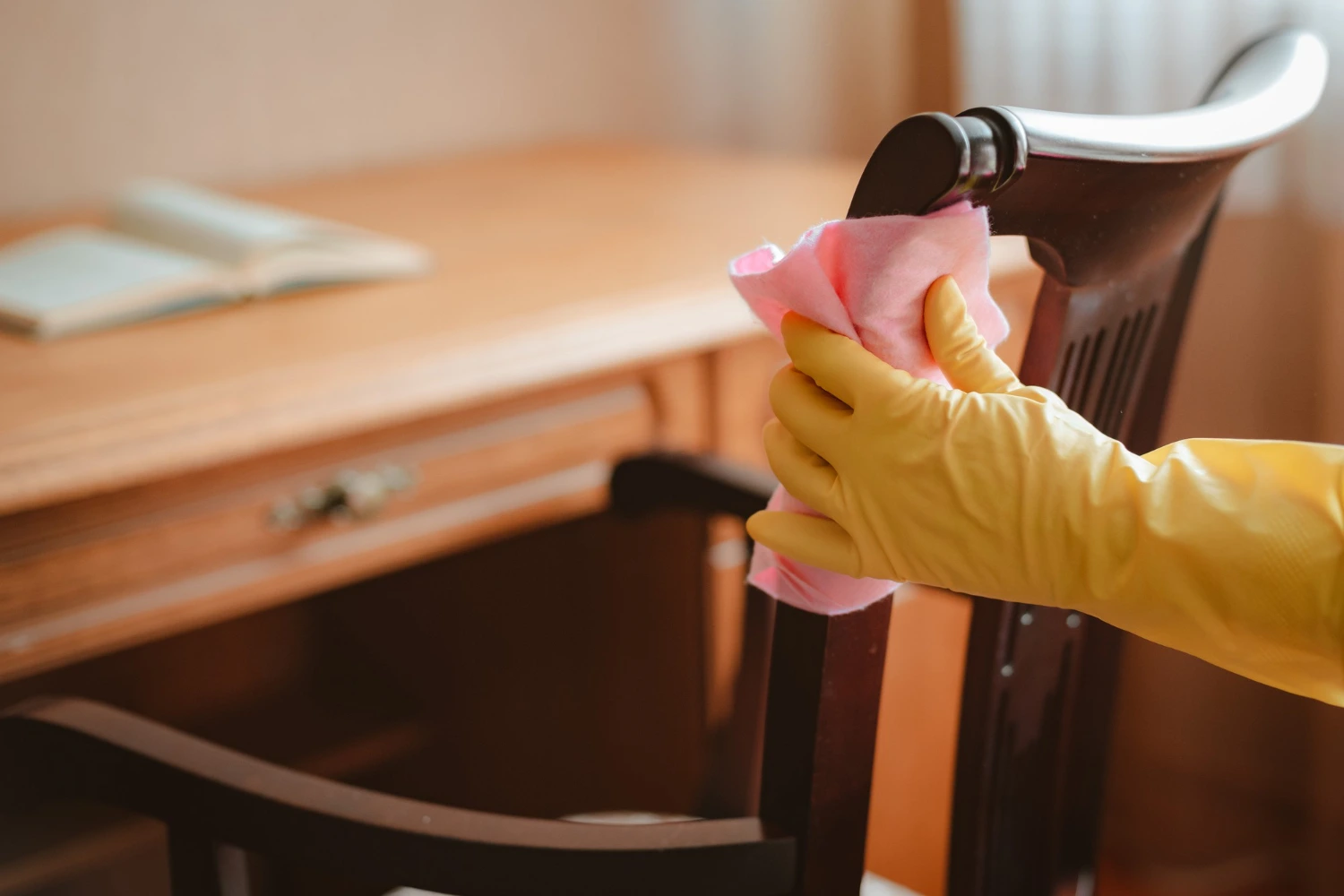 Gloved hand wiping the top rail of a wooden restaurant chair with a microfibre cloth