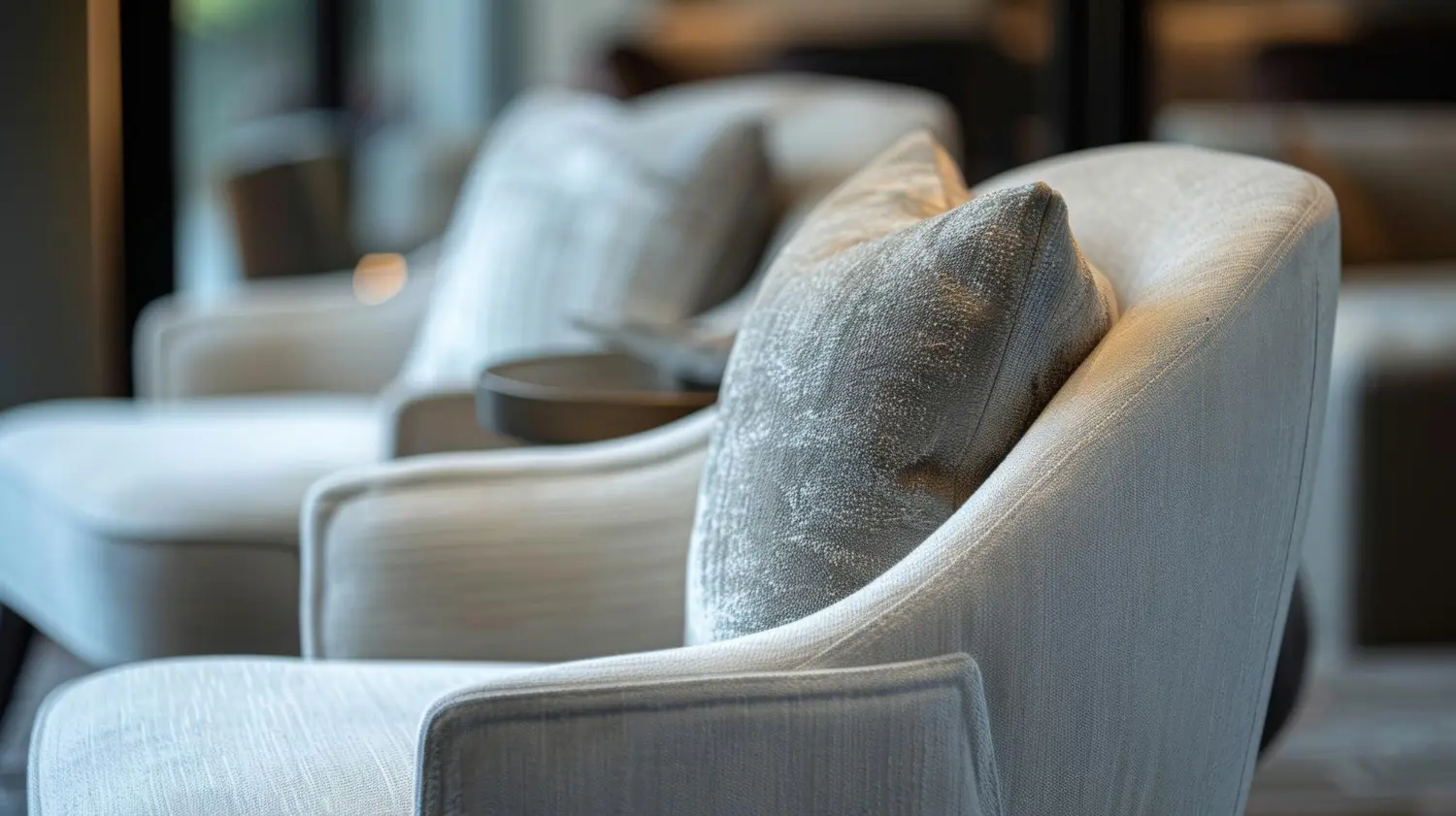 Upholstered lounge armchairs in pale grey fabric forming a separate seating zone in a restaurant