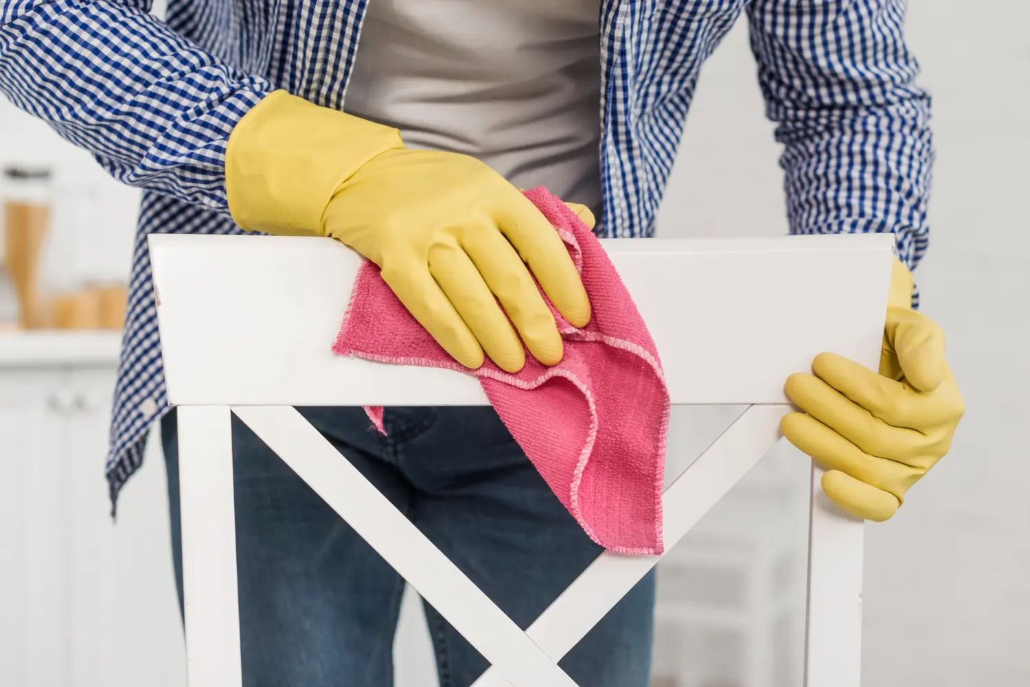 Gloved hands wiping the painted timber frame of a restaurant chair with a microfibre cloth