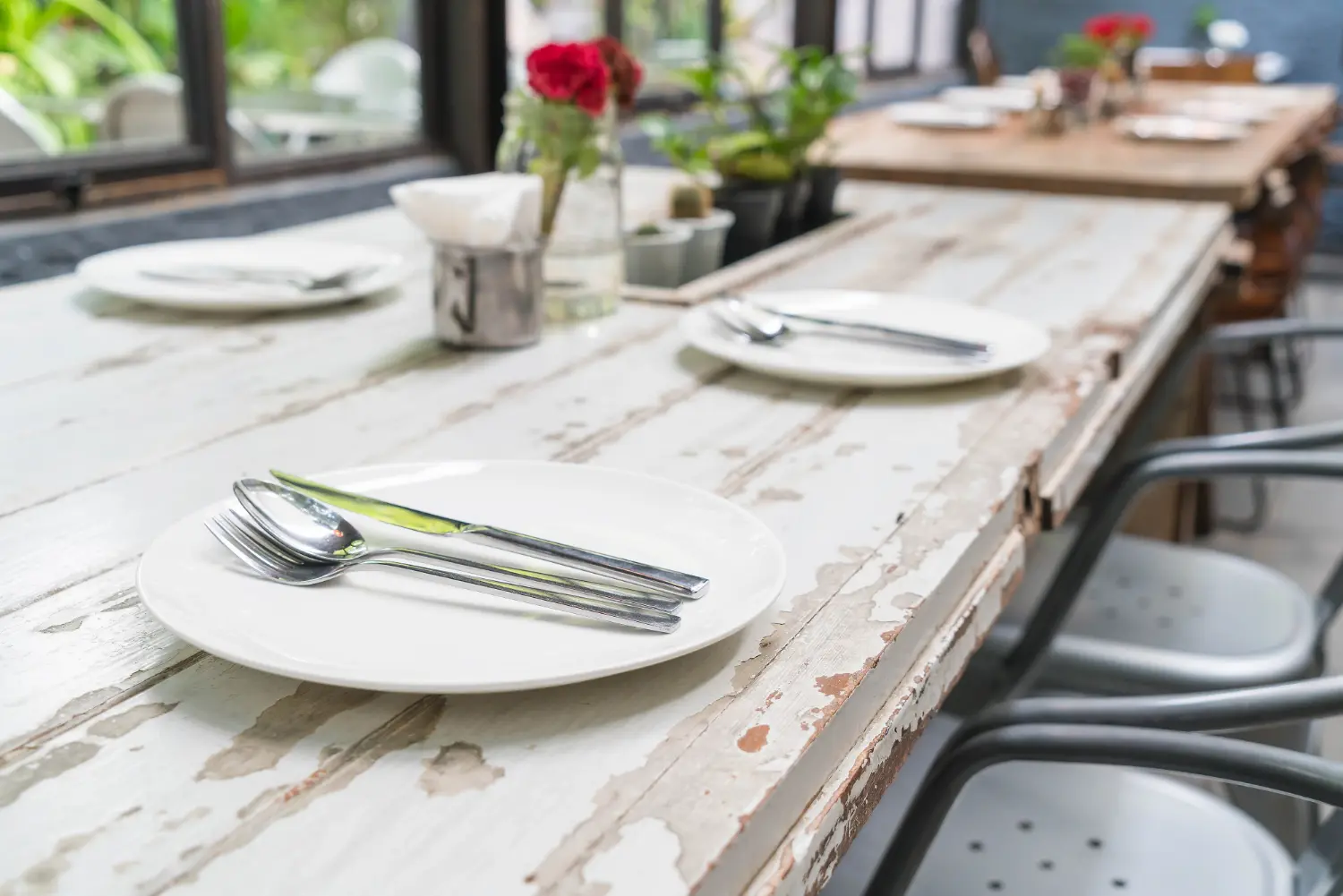 Long rectangular communal restaurant table in weathered timber, laid with plates and cutlery