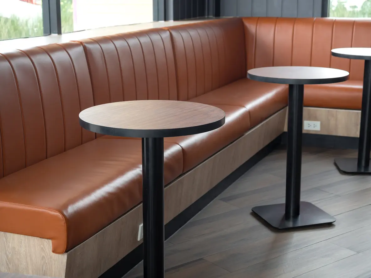 L-shaped corner banquette in fluted tan leather with round tables on column bases