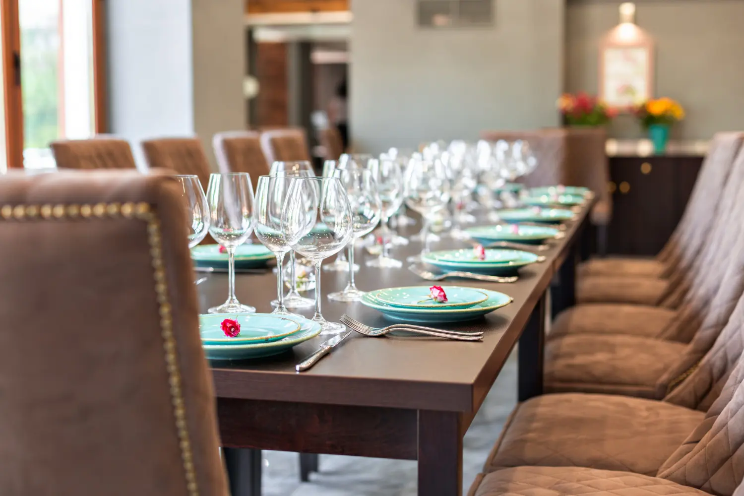 Long rectangular restaurant table set with glassware and upholstered chairs along both sides and at the end