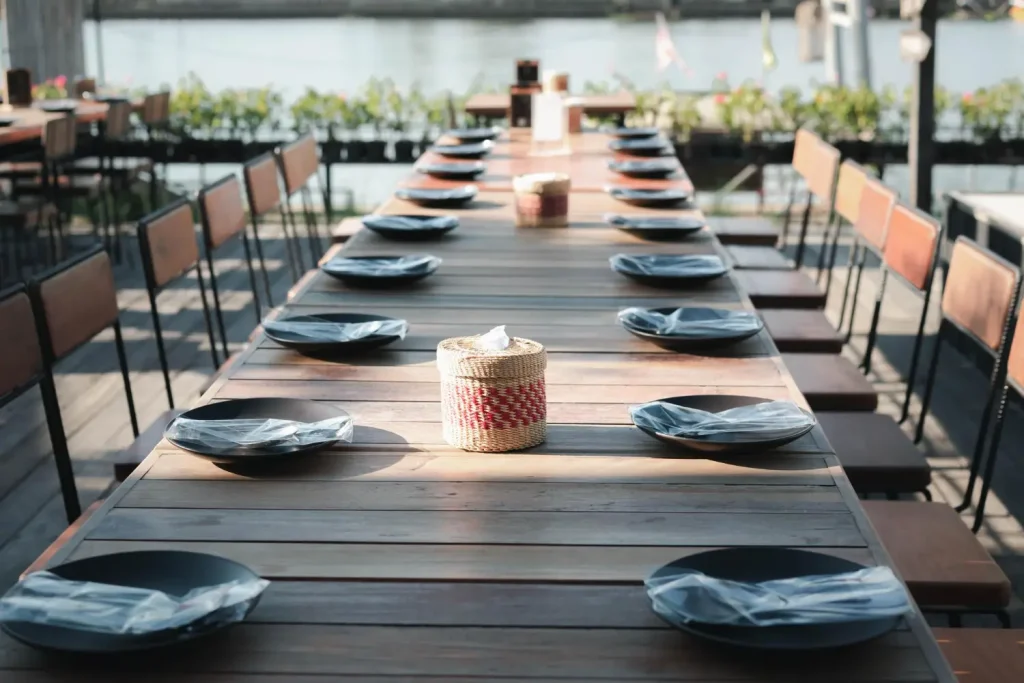 Long communal restaurant table laid with evenly spaced place settings and side chairs down both sides