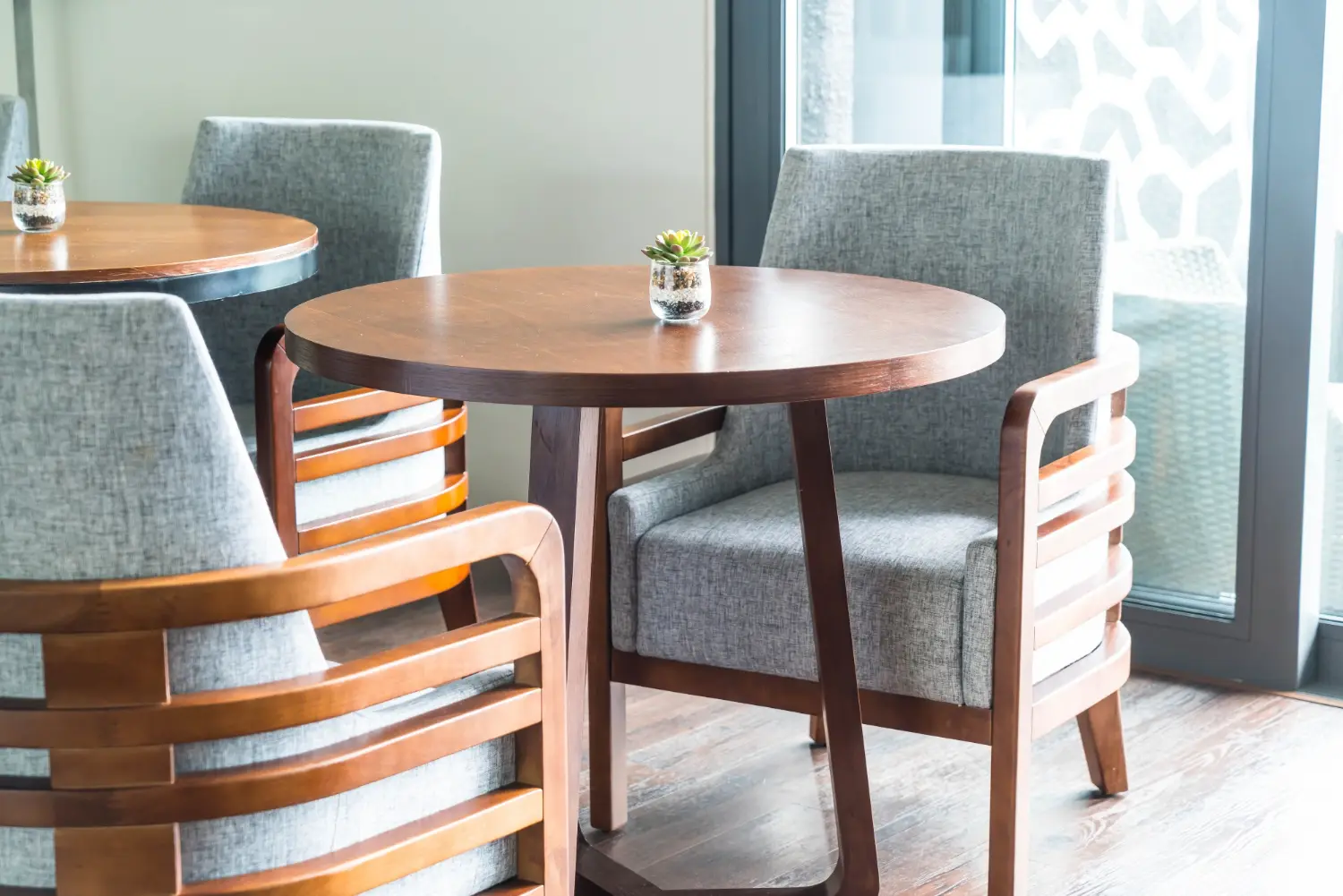 Small round timber restaurant table on a three-leg base between two grey upholstered armchairs